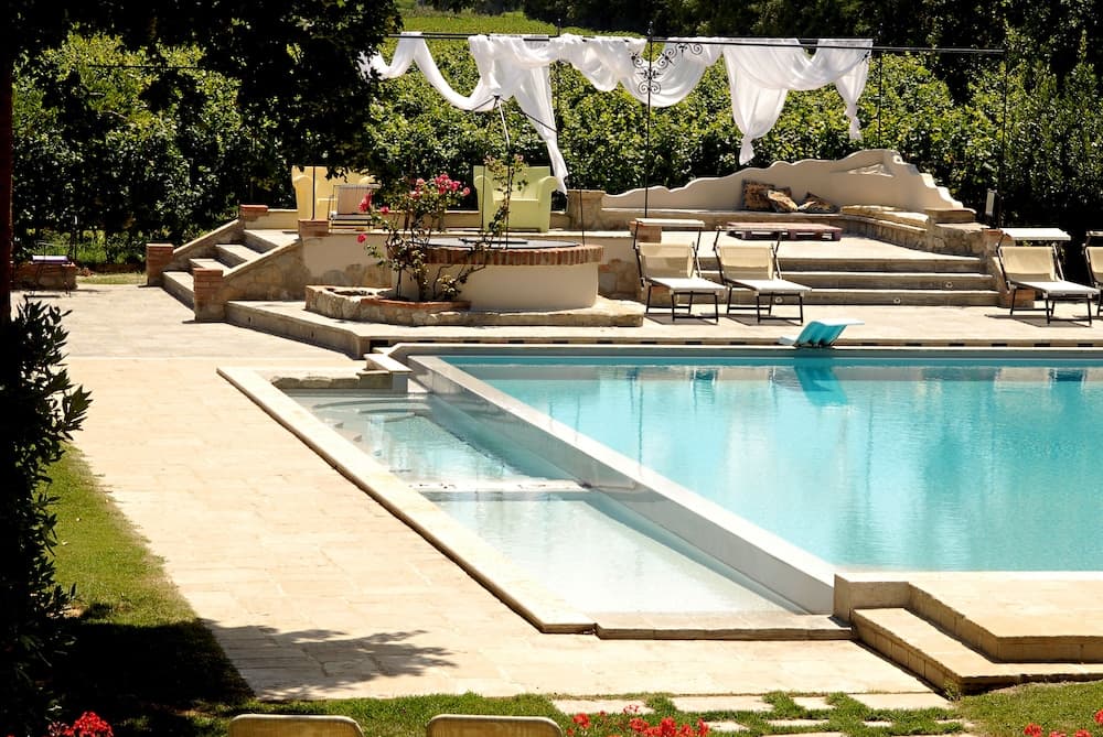 A serene outdoor poolside retreat features a tranquil rectangular pool surrounded by stone pathways, lounge chairs, and lush greenery, perfect for a relaxing vacation getaway.