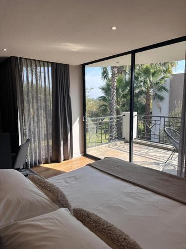 A cozy bedroom with a neatly made bed overlooks a serene balcony adorned with palm trees, ideal for travelers seeking relaxation in a tropical resort setting.
