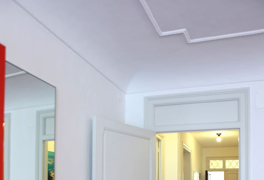 A serene hallway with white walls, decorative molding, and a mirror reflects the inviting ambiance of an elegant interior, perfect for travelers seeking a cozy accommodation experience.