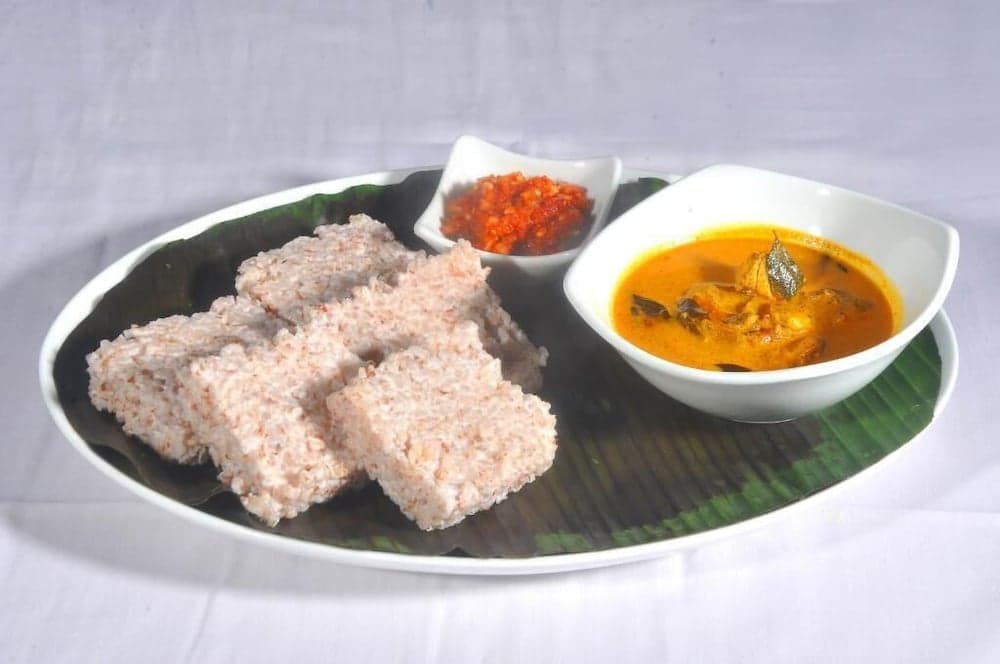 A vibrant plate featuring steamed rice cakes, a rich curry bowl, and a spicy condiment served on a banana leaf evokes the traditional culinary experience of Southeast Asian cuisine, perfect for travelers exploring local food culture.
