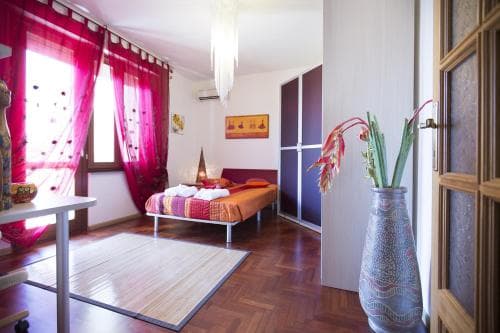 A cozy bedroom with vibrant red curtains, wooden floors, and eclectic decor creates an inviting atmosphere, perfect for travelers seeking a warm and artistic accommodation experience.