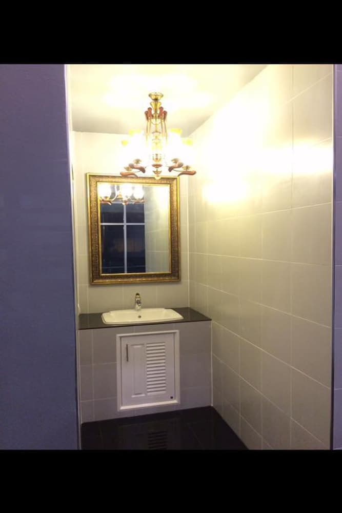 A cozy bathroom with tiled walls, a vanity sink, a gold-framed mirror, and an elegant chandelier creates a warm and inviting atmosphere, perfect for travelers seeking comfort in their accommodations.
