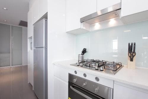 A sleek, modern kitchen with white cabinetry, stainless steel appliances, and a glossy backsplash creates a clean and inviting atmosphere, ideal for travelers seeking a comfortable self-catering accommodation.