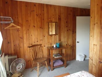 A cozy cabin interior with wood-paneled walls, a rustic chair, small table with books and a mug, evokes a serene retreat atmosphere ideal for travelers seeking a quiet getaway.