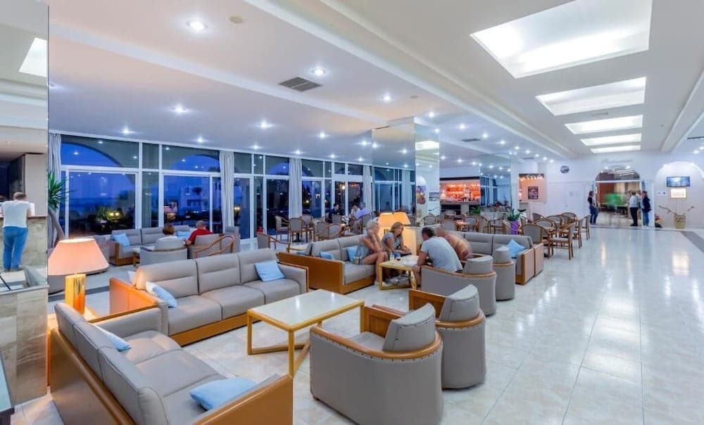 A spacious hotel lobby with modern beige sofas, wooden tables, and large windows offers a cozy and inviting atmosphere for travelers to relax and socialize.