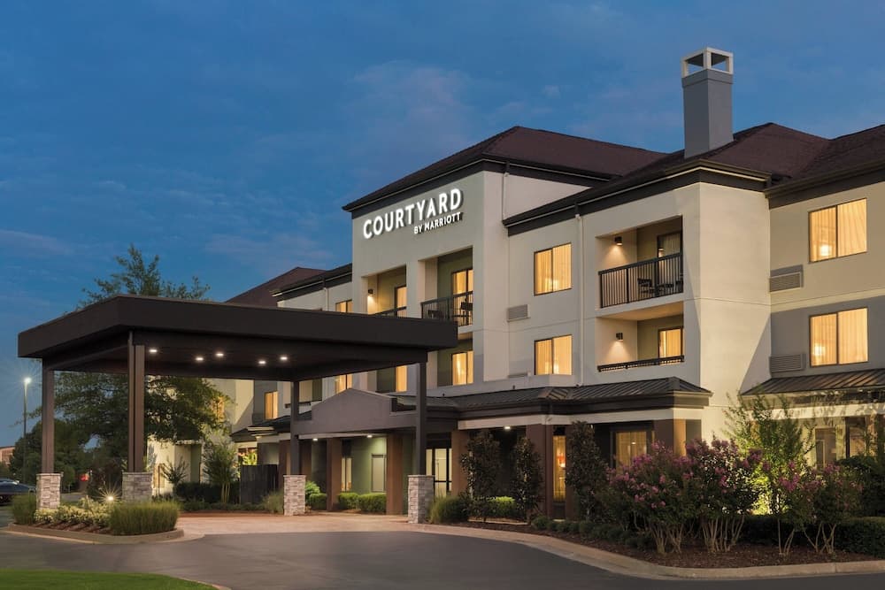 A Courtyard by Marriott hotel glows warmly under twilight skies, featuring balconies, lush landscaping, and a welcoming entrance canopy, ideal for travelers seeking comfort and convenience.