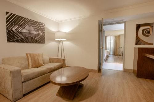 A cozy hotel suite features a plush beige sofa, wooden coffee table, modern artwork, and warm lighting, creating an inviting atmosphere ideal for travelers seeking comfort and relaxation.