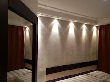 A cozy hotel room features warm lighting on textured walls, plush bedding, and rich red curtains, creating an inviting atmosphere ideal for travelers seeking comfort and relaxation.