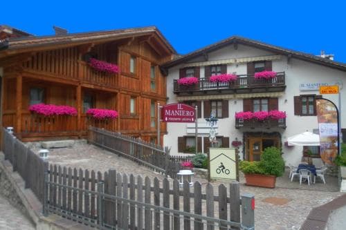 A charming alpine village scene features rustic wooden houses adorned with vibrant pink flowers, a cozy café with outdoor seating, and a quaint atmosphere perfect for a serene mountain getaway.