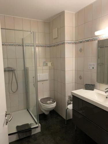 A compact hotel bathroom features tiled walls, a glass-enclosed shower, a toilet, and a sink with a mirror, offering a functional space for travelers seeking cleanliness and convenience.
