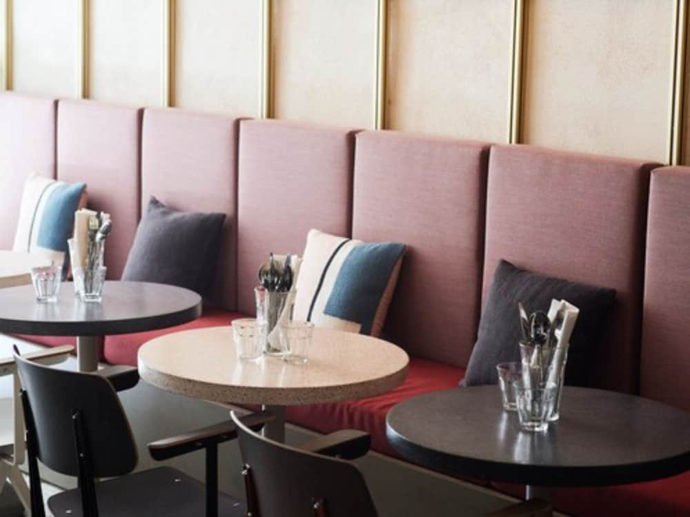 A cozy café interior features plush pink booths with cushions, small round tables set with glassware and cutlery, creating an inviting atmosphere perfect for travelers seeking a relaxing spot to dine or work.