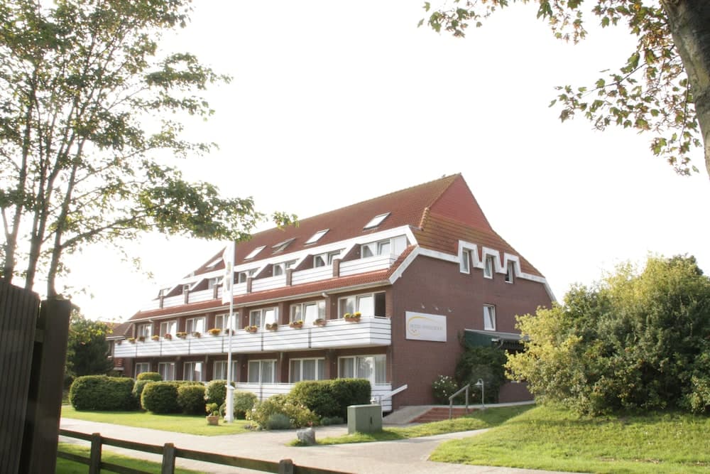 A serene residential building with red-tiled roofs and flower-adorned windows stands amidst lush greenery, ideal for travelers seeking a peaceful suburban retreat.