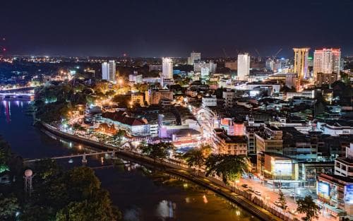 A vibrant night scene captures a bustling cityscape illuminated by colorful lights along a riverbank, ideal for urban exploration and nightlife enthusiasts.