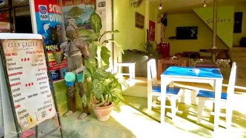 A cozy indoor café bathed in sunlight features vibrant plants, colorful furniture, and a menu board, creating a welcoming atmosphere ideal for travelers seeking a relaxing spot to unwind and plan their adventures.