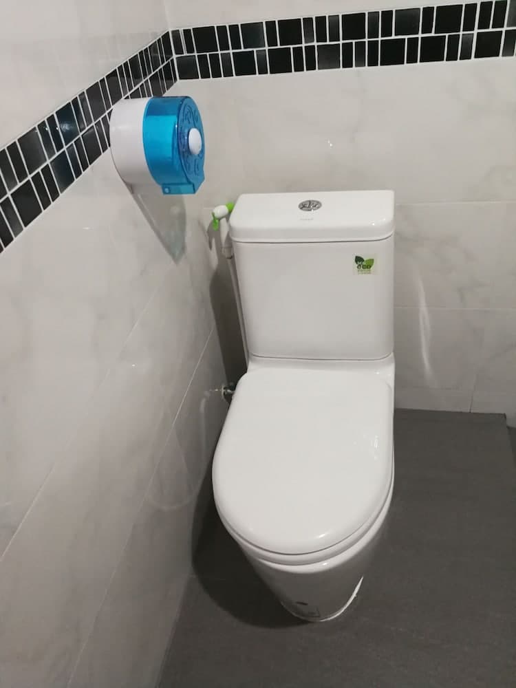 A clean, modern bathroom features a white toilet with a bidet attachment against marble-like tiles and a black accent border, ideal for travelers seeking hygiene-focused accommodations.