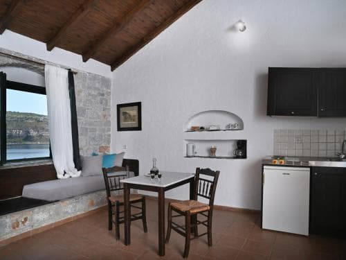 A cozy, rustic apartment with terracotta floors, wooden beams, and a scenic window view offers a tranquil retreat for travelers seeking comfort in a charming setting.