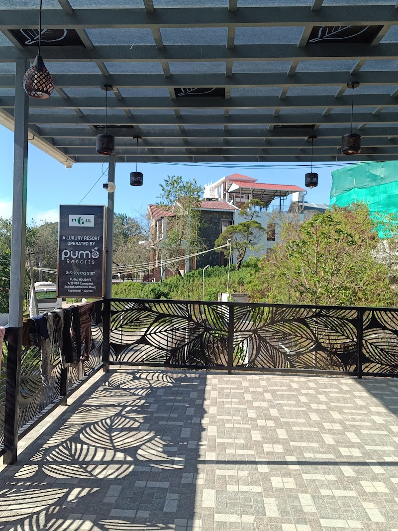 A serene outdoor patio at a luxury resort in Kodaikanal, Tamil Nadu, features artistic leaf-patterned railings, hanging lanterns, and lush greenery, ideal for travelers seeking relaxation and scenic views.