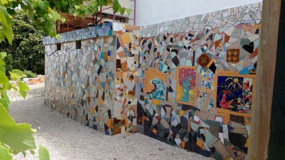 A vibrant mosaic-covered wall in an outdoor urban setting, adorned with colorful tiles and framed artworks, creates a lively artistic atmosphere ideal for cultural exploration and photography.