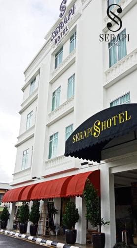 A charming white hotel with red awnings and lush greenery exudes elegance in an urban setting, ideal for travelers seeking a comfortable stay with a touch of sophistication.