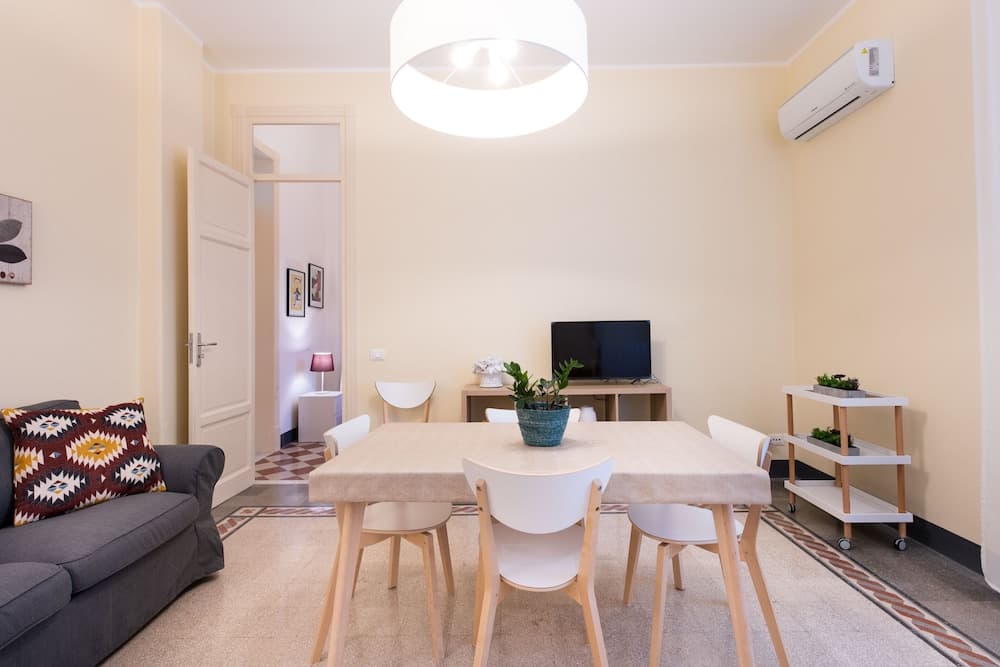 A cozy apartment living room features a modern dining table set, a comfortable sofa with patterned cushions, and soft yellow walls, creating an inviting atmosphere ideal for short-term rentals or vacation stays.