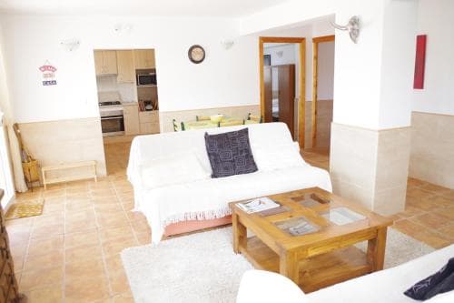 A cozy apartment interior featuring a white sofa, wooden coffee table, tiled floors, and an open kitchen area, ideal for travelers seeking comfortable self-catering accommodations.