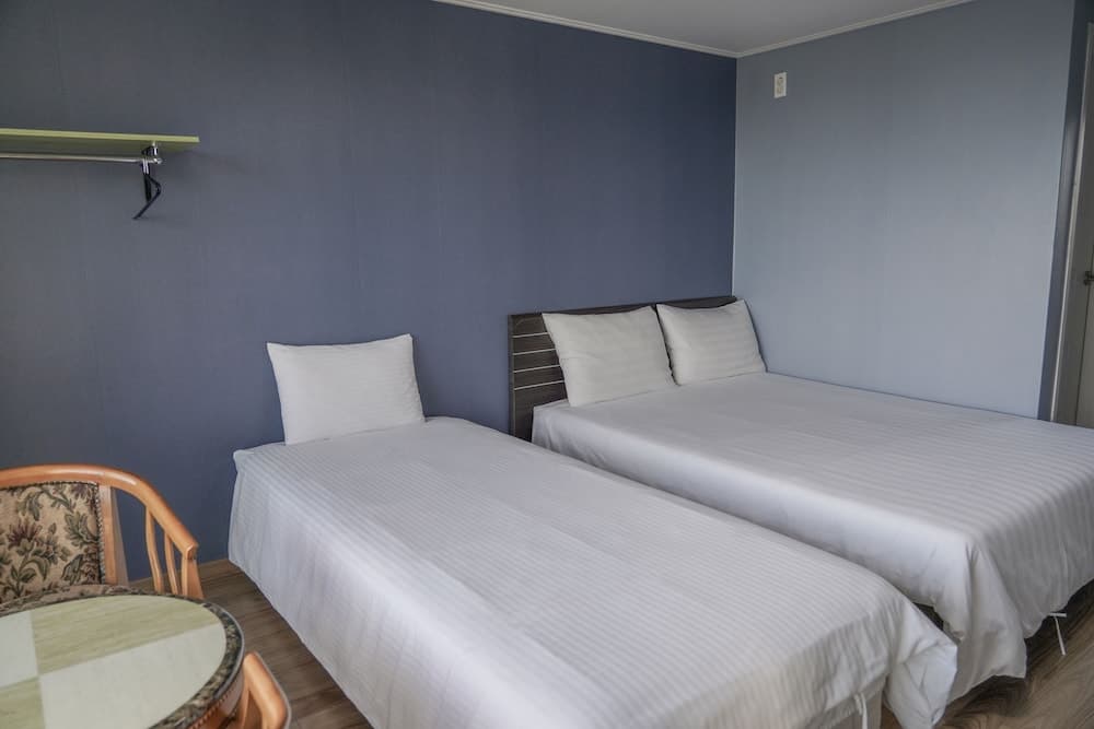 A cozy hotel room with two neatly made beds against blue walls, a small table with chairs, and a calm atmosphere ideal for travelers seeking comfort and simplicity.