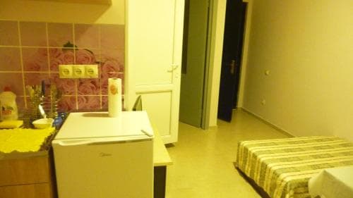 A cozy studio apartment features a small fridge, floral wallpaper, and a neatly made bed, ideal for budget-friendly travelers seeking comfort in a compact space.
