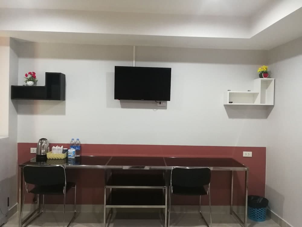 A cozy hotel lounge features a sleek table with chairs, a mounted TV, decorative shelves with flowers, and refreshments, ideal for travelers seeking a comfortable spot to relax or work.