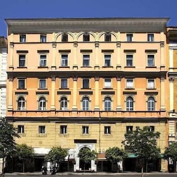 A grand, sunlit European hotel facade with arched windows and lush greenery evokes a serene urban retreat, ideal for travelers seeking a classic city stay experience.