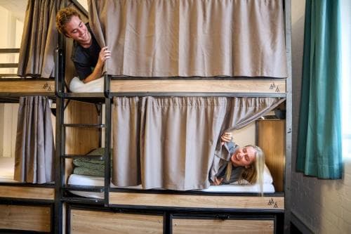 Travelers enjoy cozy moments in a modern hostel's bunk beds, featuring privacy curtains and storage drawers, ideal for budget-friendly adventures.