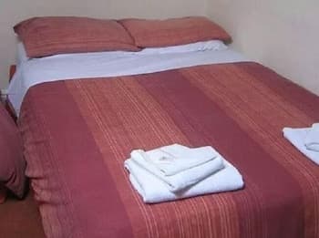 A cozy hotel room features a neatly made bed with red striped bedding, folded white towels, and a warm, inviting atmosphere ideal for travelers seeking comfort and simplicity.