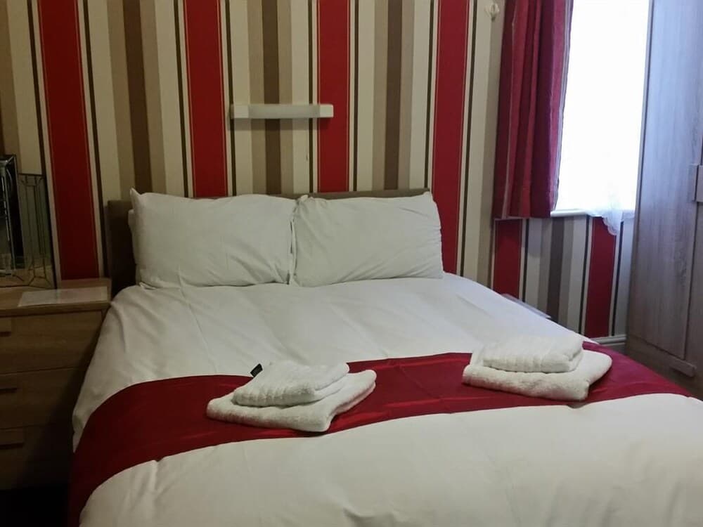 A cozy hotel room features a neatly made bed with white linens and red accents, set against striped wallpaper, creating a warm and inviting atmosphere ideal for travelers seeking comfort.