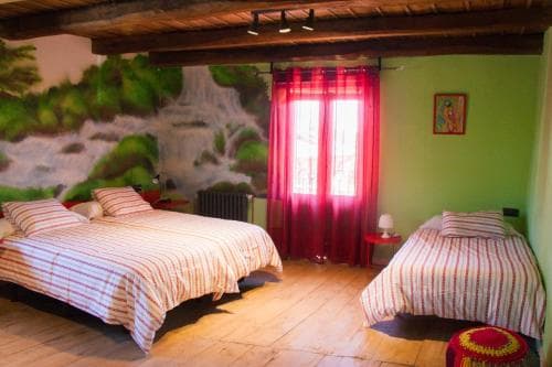 A cozy rustic bedroom with wooden beams, vibrant red curtains, and a mural of a waterfall creates a serene atmosphere, ideal for travelers seeking a charming and relaxing accommodation experience.