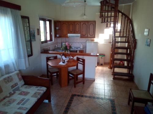 A cozy apartment interior features a tiled floor, wooden furniture, a spiral staircase, and a kitchenette, creating a warm and inviting atmosphere ideal for travelers seeking comfortable self-catering accommodations.