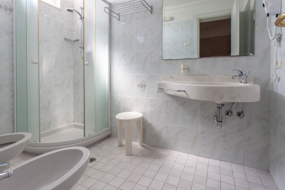 A clean, modern bathroom with marble tiles, a glass-enclosed shower, white sink, and a small stool creates a serene atmosphere ideal for travelers seeking comfort and hygiene in their accommodations.