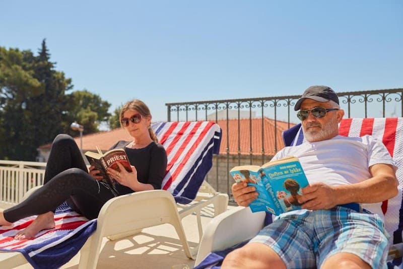 Relaxing on sun loungers under a clear blue sky, a couple enjoys reading books on the terrace of a villa in Dubrovnik, Croatia, showcasing a serene vacation spot ideal for leisure travelers.