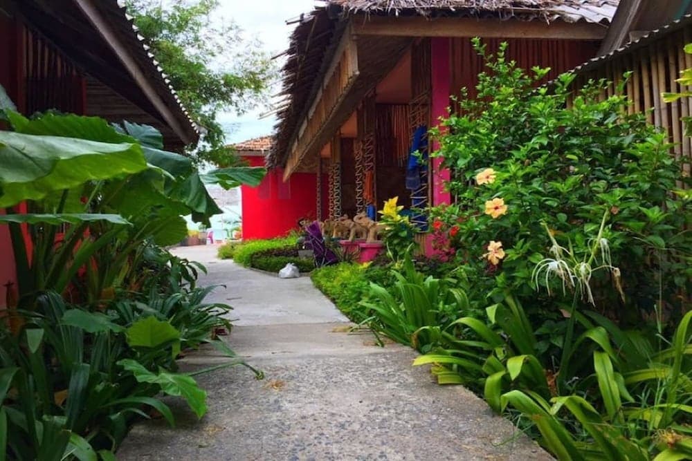 A serene tropical pathway lined with lush greenery and vibrant flowers leads to charming thatched-roof bungalows, ideal for a relaxing eco-retreat experience.