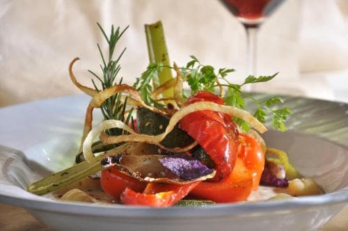 A beautifully plated dish of roasted vegetables garnished with herbs and crispy onions sits invitingly on a table, perfect for culinary enthusiasts exploring gourmet dining experiences.