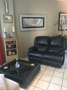 A cozy living room with black leather sofas, a glass coffee table, and tiled flooring exudes warmth and comfort, ideal for travelers seeking a relaxing retreat during their stay.