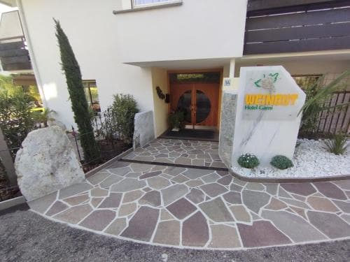 A welcoming entrance to a cozy hotel features a stone-paved pathway, lush greenery, and a prominent sign, ideal for travelers seeking a serene and inviting stay.
