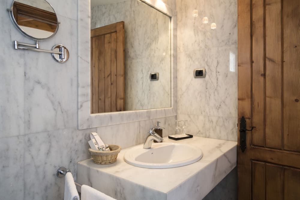 A luxurious bathroom with marble walls and countertop exudes elegance, featuring a sleek sink, wooden door, modern fixtures, and ambient lighting, ideal for travelers seeking upscale accommodations.