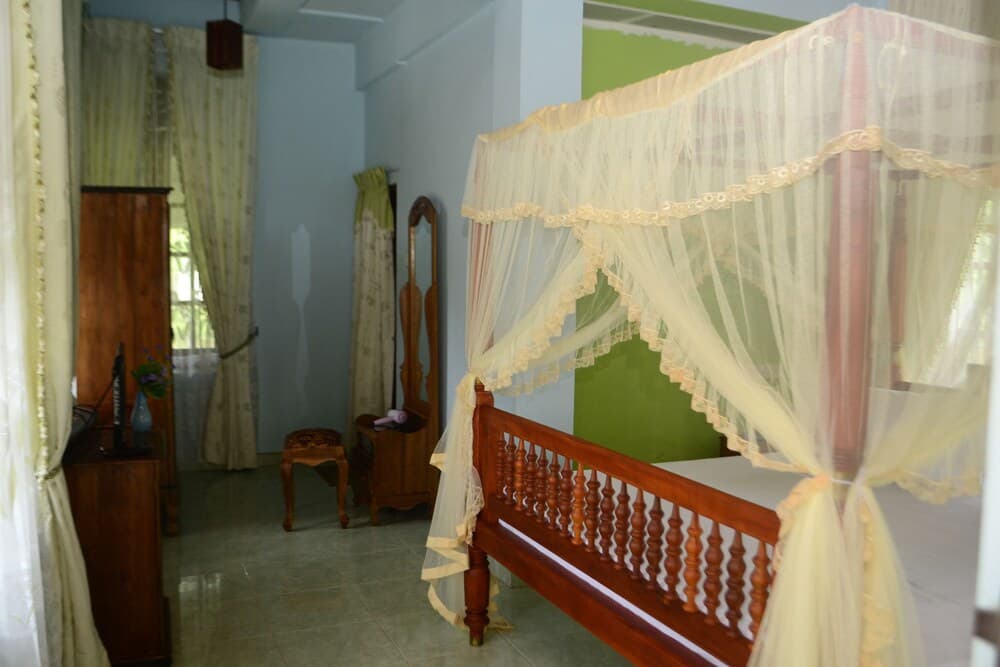A cozy bedroom with a wooden four-poster bed draped in lace mosquito netting, vintage furniture, and soft curtains creates a serene retreat ideal for travelers seeking a tranquil accommodation experience.
