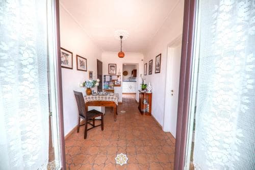 A cozy dining area with terracotta-tiled floors, framed artwork, and lace curtains frames an inviting home interior perfect for travelers seeking a warm, homely stay.