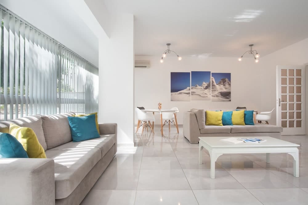 A bright, modern living room with sleek furniture, colorful cushions, and large windows exudes a cozy yet stylish atmosphere, perfect for travelers seeking a comfortable and contemporary accommodation space.