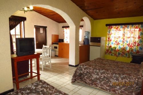 A cozy hotel room with vibrant yellow walls, floral curtains, tiled floors, and simple furnishings offers a comfortable stay for travelers seeking a budget-friendly retreat.