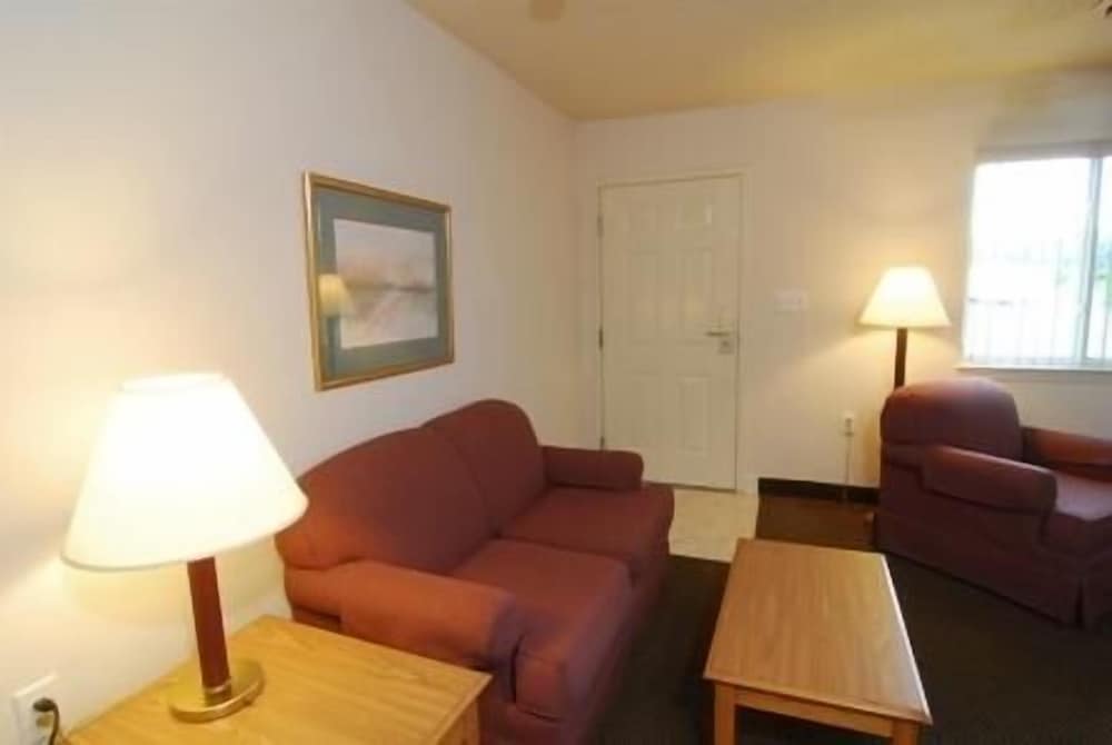 A cozy hotel room features a warm ambiance with plush red sofas, wooden tables, and soft lighting, ideal for travelers seeking comfort and relaxation during their stay.