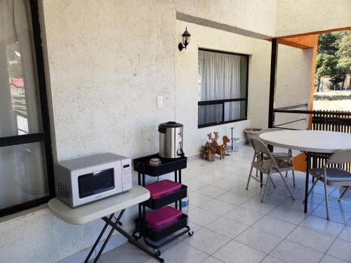 A cozy outdoor patio area features a tiled floor, a round table with chairs, a microwave on a stand, and a coffee maker on a cart, creating a relaxed and functional space ideal for travelers seeking a comfortable self-catering stay.