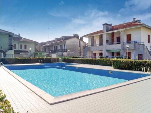 A serene residential area features a vibrant blue swimming pool surrounded by well-maintained hedges and multi-story apartment buildings under a clear sky, ideal for family vacations seeking relaxation and leisure.