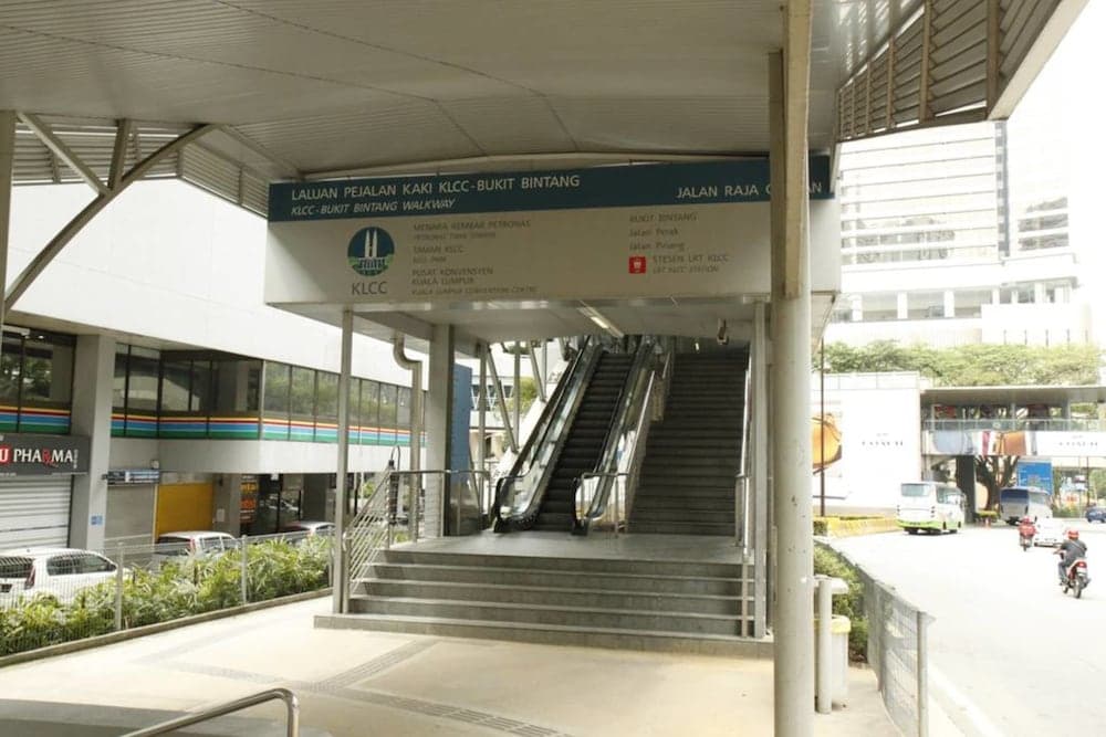 A bustling urban walkway entrance in Kuala Lumpur features escalators and stairs under a covered structure, ideal for travelers exploring the city's modern architecture and transportation hubs.