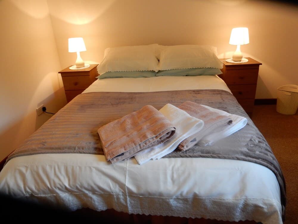 A cozy hotel room features a neatly made bed with folded towels, wooden bedside tables with lamps, and a warm ambiance ideal for travelers seeking comfort and relaxation.
